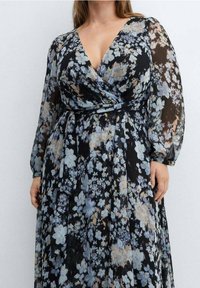 Vestido maxi floral en negro con flores azules y beige. Tejido transparente, escote en V profundo, mangas largas, cintura fruncida, diseño de falda fluida.