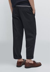 Donkerblauwe broek met een ontspannen pasvorm, opgerolde manchetten, zijzakken en een nette afwerking. Gepaard met bruine leren schoenen.