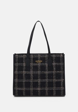 Torba typu tote w czarno-białą kratkę z podwójnymi uchwytami i złotym logo „GUESS EST 1981” na przednim środku.