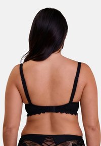 Zwarte kanten beha met gegolfde randen, verstelbare bandjes en een haak-en-oogsluiting. De achtergrond is effen wit voor contrast.