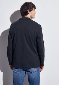 Svart strukturerad kavaj med skräddarsydd passform, singel bakslits och knäppte ärmar, kombinerad med ljusblå casual jeans.
