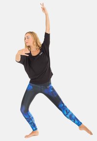 Black, loose-fitting top paired with tight-fitting leggings featuring a blue geometric pattern. The model is in a dynamic pose.