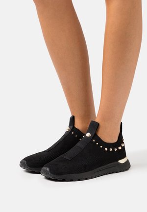 Scarpe slip-on in maglia nera con tomaia testurizzata, caratterizzate da borchie dorate come dettagli e suola in gomma per la trazione.
