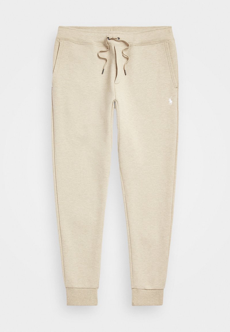 Bež jogger hlače s ožjim pasom, stranskimi žepi, manšetami na gležnjih in majhnim belim logotipom na zgornjem levem stegnu.