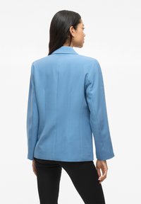 Svetlomodrý blazer so štruktúrovaným dizajnom, klopovým golierom, dlhými rukávmi, hladkou textúrou a šitými detailmi na zadnej strane, pripomínajúcimi krajčírsku prácu.