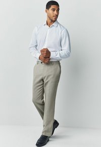 White long-sleeve button-up shirt paired with light gray patterned dress pants and black leather shoes. Simple, tailored design.
