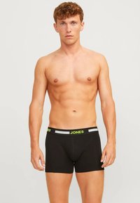 Zwarte boxershorts met een groen logo op de tailleband. Een gladde textuur en een nauwsluitende pasvorm, met contrasterende stiksels voor extra detail.