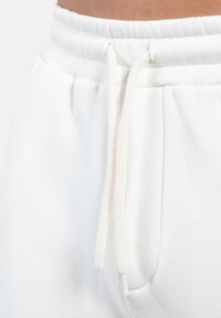 Joggers de algodón blancos con cintura elástica, que cuentan con un cierre de cordón. Bolsillos laterales y una textura suave y lisa.