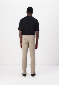 Beiga byxor med rak passform, två bakfickor med dragkedjor, tillsammans med en enkel svart t-shirt. Svarta sneakers med vita sålar.