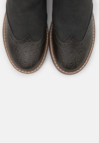 Black leather ankle boots with perforated detailing, scalloped edges, and brown stitching around the sole. Smooth texture.