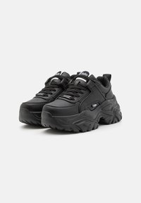 Black sneakers with a thick rubber sole, smooth synthetic upper, lace closures, and a padded collar. Features logo accents on the tongue.