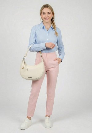 Nainen seisoo pukeutuneena vaaleansiniseen ruudulliseen paitaan, vaaleanpunaisiin korkeavyötäröisiin housuihin, valkoisiin tennareihin ja kantaa valkoista puolikuun muotoista käsilaukkua käsivarrella.