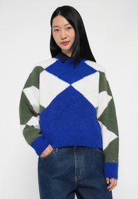 Blauer, weißer und grüner Pullover mit Rauten-Muster, mit gerippten Bündchen und Saum. Material aus Wollmischung, kragenloses Design und oversized Schnitt.