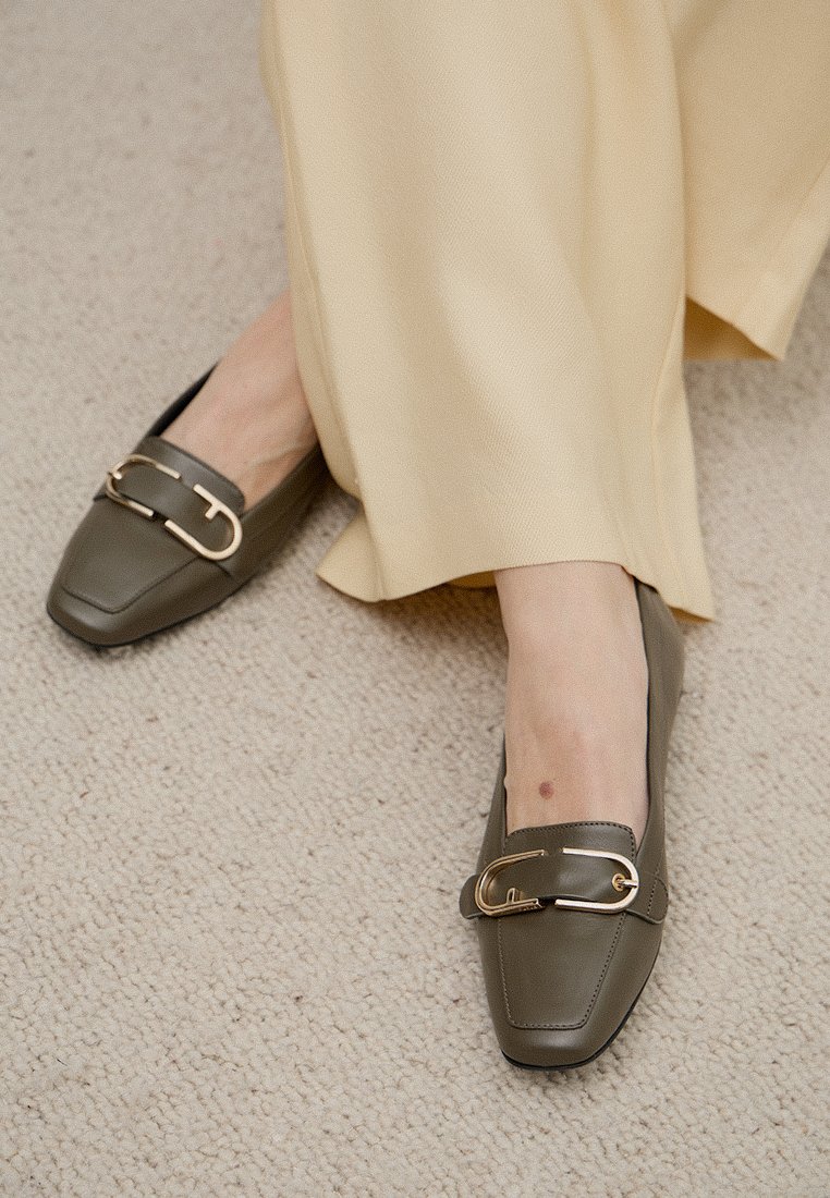 Mocassins vert olive avec un bout carré et un accent de quincaillerie décorative en ton doré. Fini en cuir lisse avec une semelle plate.