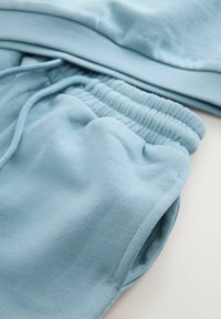 Ljust blå sweatshirt och sweatpants-set tillverkat av mjuk bomull. Har ribbade muddar och elastisk midjeband med justerbara snörningar.