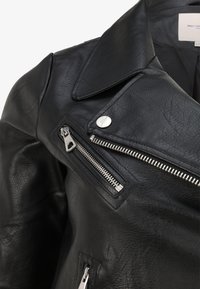 Giubbotto da moto in pelle nera con colletto a punte, cerniere argentate e finitura testurizzata. Include tasche con cerniera e dettagli a scatto.