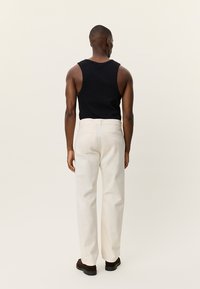 Μαύρο εφαρμοστό φανελάκι και εκρού παντελόνια φαρδιάς γραμμής. Τα παντελόνια έχουν ορατές ραφές και πίσω τσέπες. Τα παπούτσια είναι σκούρα με υφή στην επιφάνεια.