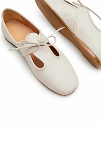 Scarpe in pelle bianca con punta arrotondata, dettagli ritagliati e lacci. La soletta è marrone chiaro, offrendo un design piatto e classico.