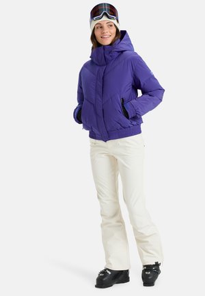 Doudoune isolante violette avec un col haut et des poignets élastiques, associée à un pantalon de neige blanc et des bottes de ski noires. Comprend un bonnet en tricot et des lunettes de ski.