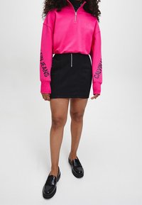 Růžová mikina na zip s potiskem "Calvin Jeans" na rukávech, kombinovaná s černou denimovou minisukní a černými mokasíny.