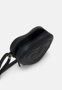 Mała, czarna, sercowa torebka na ramię z zamkiem błyskawicznym, złotym zapięciem na pasku oraz poduszkowanym, koncentrycznym wzorem serca z przodu.