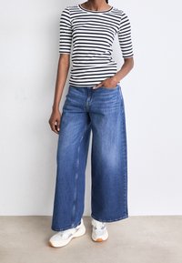 Randig svart och vit tröja med korta ärmar, kombinerad med vida blå denimjeans och vita sneakers med grå detaljer.