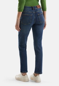 Strakke blauwe denim jeans met een zachte textuur, vijf zakken en een bruine leren label op de tailleband, gecombineerd met witte sneakers.