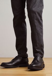 Scarpe eleganti in pelle nera con finitura liscia, punta rotonda e design con lacci. Indossate con pantaloni grigi scuri a righe sottili.