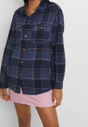 Marineblå og blåternet flannel skjorte med lange ærmer, to brystlommer og knaplukning, parret med en lyserød denimnederdel.