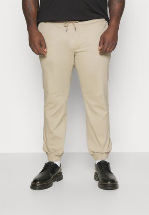 Beige drawstring pants with elastic cuffs, made from a smooth fabric, paired with black shoes featuring a chunky sole and lace-up design.