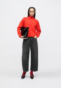 Red knit turtleneck sweater, high-waisted black wide-leg jeans, black clutch bag, and black pointy-toed heels worn with red socks.