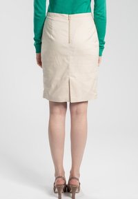 Krämfärgad pennkjol med dragkedja bak och sprund. Slät textur, knä-lång design, ihopparad med hudfärgade högklackade skor.