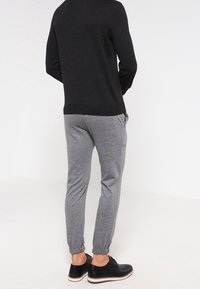 Svart tröja med rund halsringning, i kombination med grå avslappnade joggers med elastiska muddarn. Svarta skor fulländar outfiten.