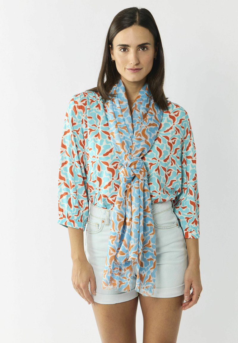 Lichtgewicht, gemusterde blouse in aqua, koraal en oranje met een losse, gestrikte sjaal. Gepaarde met hoge lichte denim short.