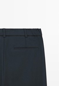 Tmavě modré kalhoty s hladkou texturou, s elastickým pasem a zadní kapsou s jednoduchým horizontálním švem.