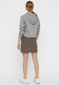Sudadera gris acortada con capucha, combinada con una falda de cuadros en tonos marrones y negros, y zapatillas deportivas blancas. Tela suave y diseño ajustado.