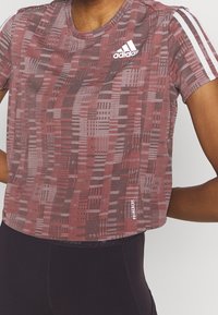 Top atletico a maniche corte rosso e grigio con scollatura rotonda, caratterizzato dal logo Adidas bianco e da tre strisce bianche sulle spalle.