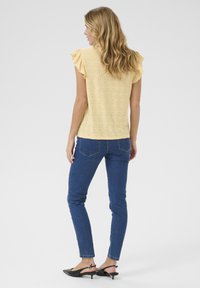 Haut jaune à manches courtes avec des manches volantées, présentant des détails en œillet. Associé à un jean skinny bleu foncé et des ballerines noires à bout pointu.