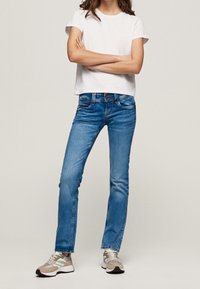 Ljusblå denimjeans med rak passform, två framfickor och knappstängning, ihop med en vit kortärmad t-shirt och grå sneakers.