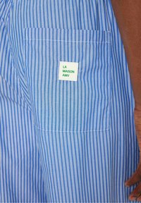 Tela a rayas azul y blanca, con un bolsillo trasero que lleva una etiqueta que dice "LA MAISON AMV". Textura suave y grosor medio.