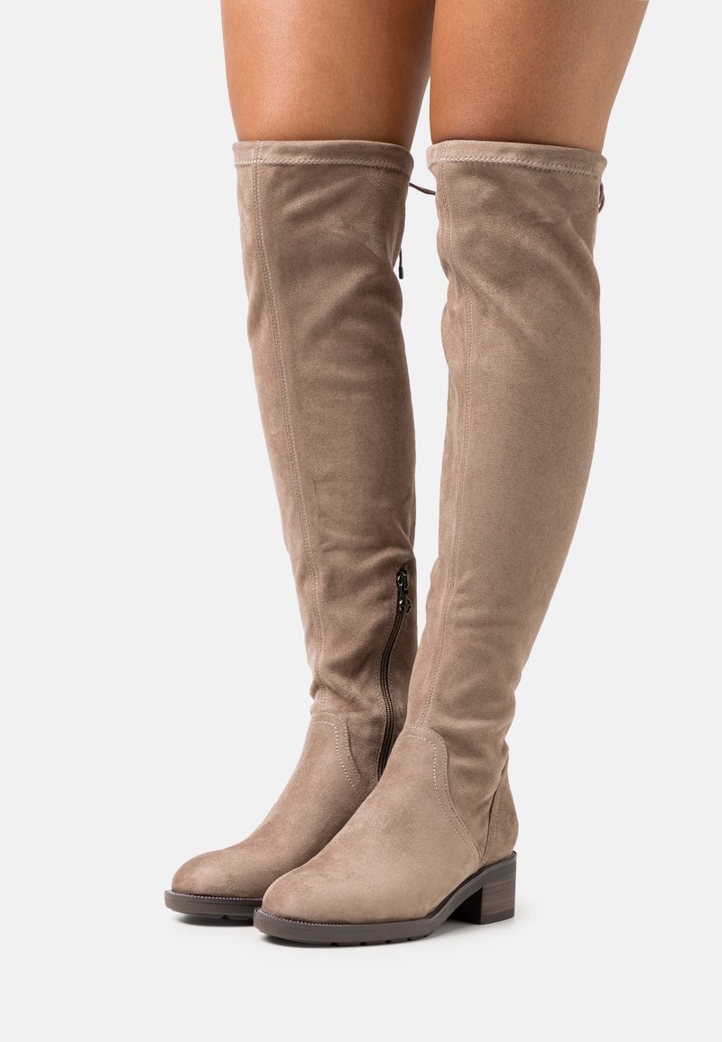 Botas por encima de la rodilla en ante beige con punta redonda y un tacón bajo. Presentan una cremallera lateral y detalles cosidos a lo largo de las costuras.