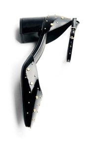 Chaussure à talon carré en cuir verni noir avec un bout pointu, ornée de clous dorés et d'une bride de cheville. Texture lisse avec une finition brillante.