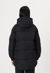 Svart puffjacka med huva, med en quiltad design, vida ärmar och sänkt nederkant. Mjukt, lätt material med en matt yta.