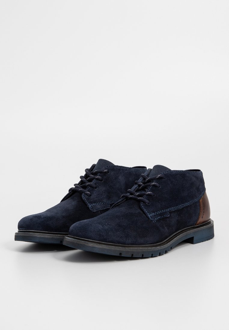 Navyblaue Wildlederschuhe mit strukturiertem Finish, Schnürdesign und braunen Lederausbesserungen an der Ferse. Schwarze Gummisohle mit Profil.