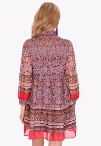 Rochie cu imprimeu floral, cu smocking adunat la decolteu, mâneci lungi cu volane și tiv în straturi, în nuanțe vibrante de mov, roșu și maro.