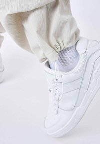 Hvide lædersneakers med tekstureret overflade og lette mesh-detaljer, kombineret med cremede joggers samlet ved anklen og hvide stribede sokker.
