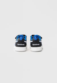 Sapatos de atletismo Reebok em preto e azul com sola branca, apresentando um cabedal liso, colarinho almofadado e detalhe com tira adesiva.