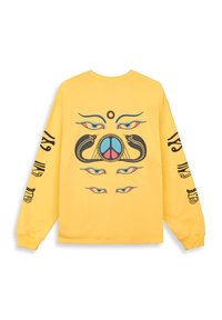 Camiseta amarilla de manga larga con una obra central que presenta ojos, serpientes y un símbolo de paz, con diseños negros a lo largo de las mangas.