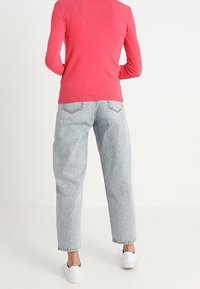 Pink knit sweater with long sleeves, paired with light grey high-waisted jeans and white sneakers, viewed from the back.