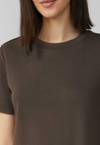 T-shirt en coton brun avec un col rond et des manches courtes, présentant une texture lisse et des détails de couture subtils.